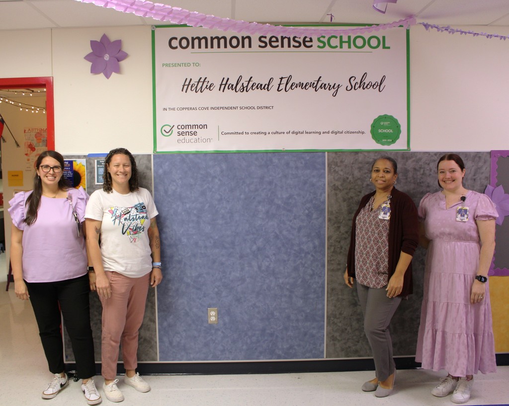 Teachers and Admin pose in front of common sense school banner