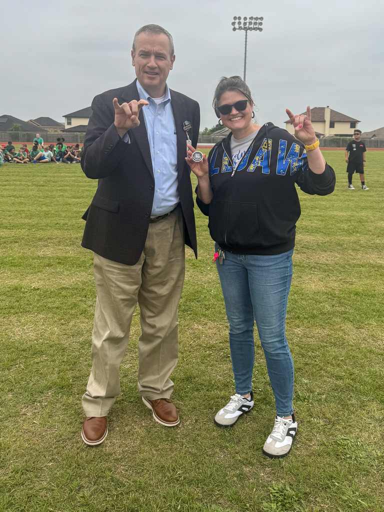 Two people smiling and holding bulldog hand sign, with a challenge coin