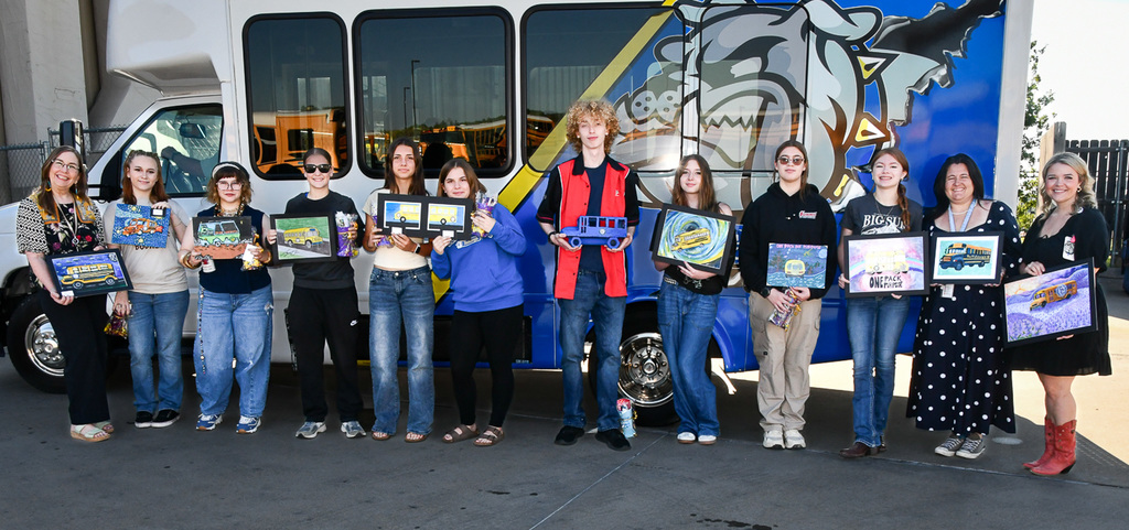 A group of students and teacher holding works of art in front of a bus