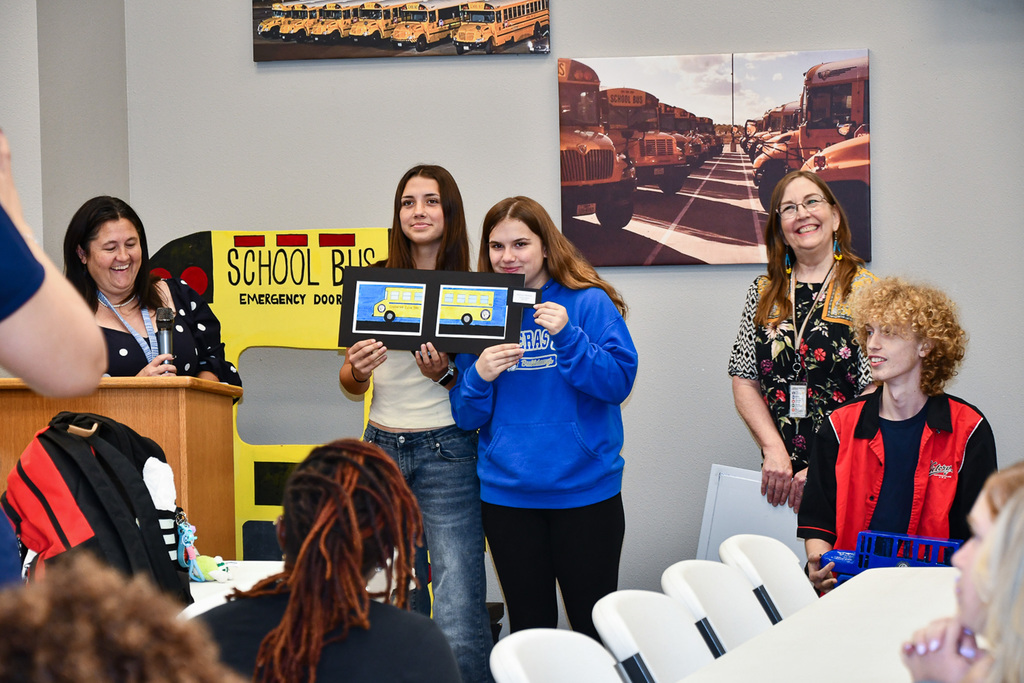 Two students holding a piece of art with smiling teachers next to them