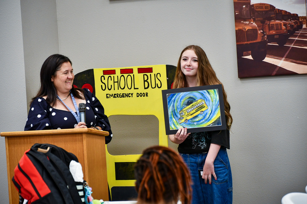 Smiling student holding work of art while smiling teacher looks on