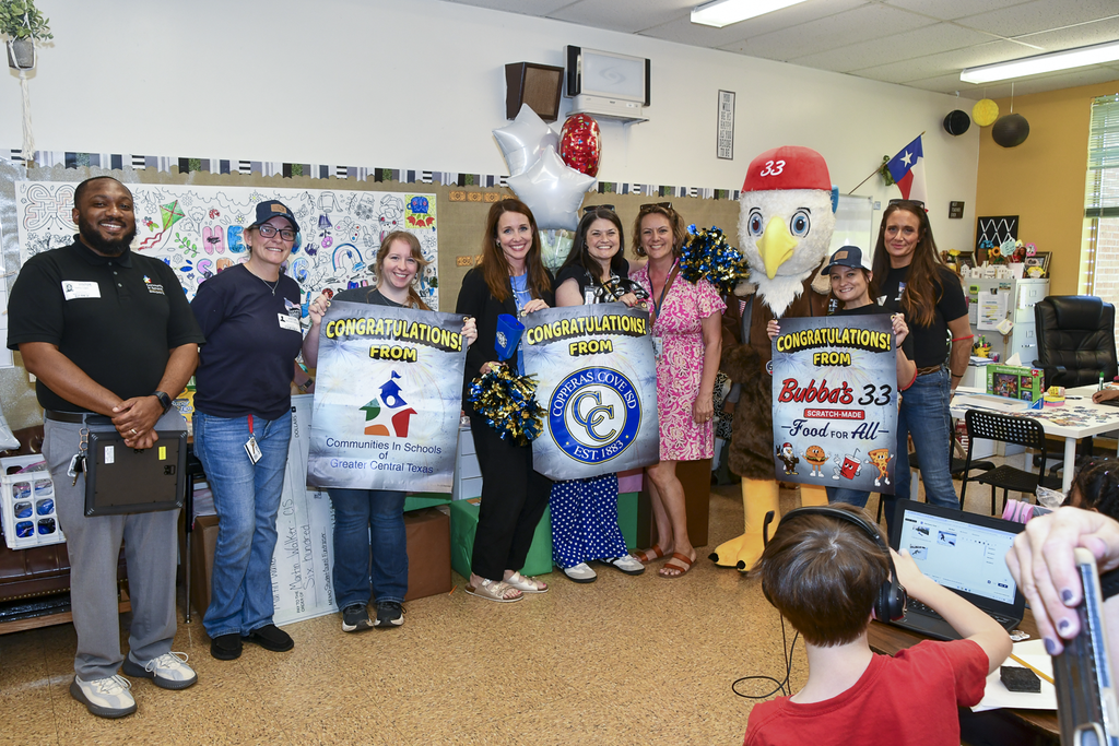 A group of people smiling and holding banners in a classroom