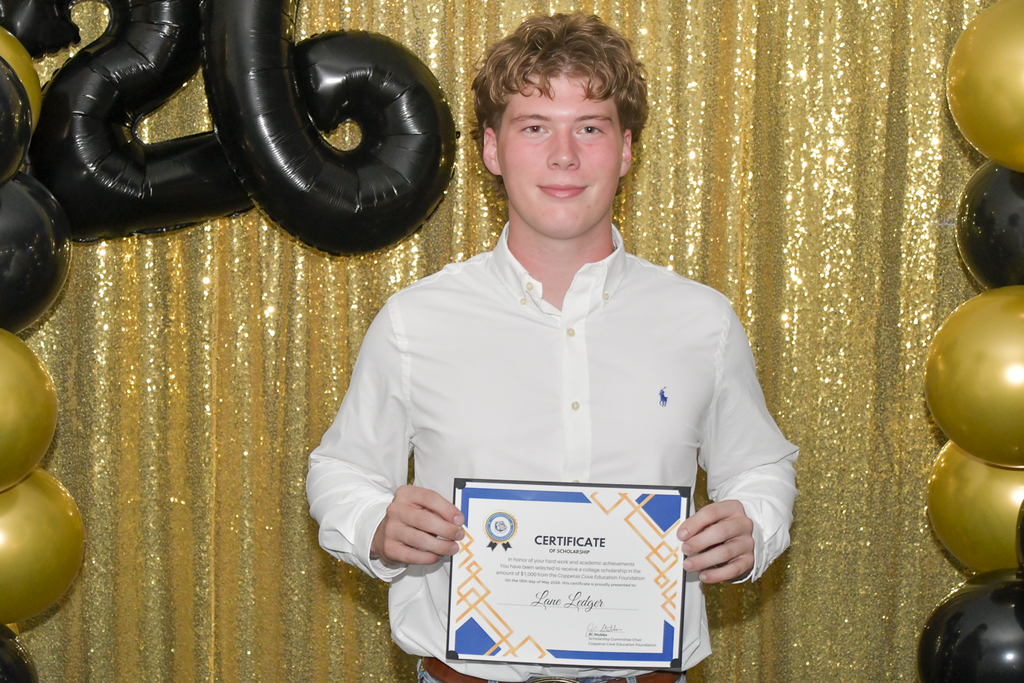 Student smiling and holding certificate in front of a backdrop