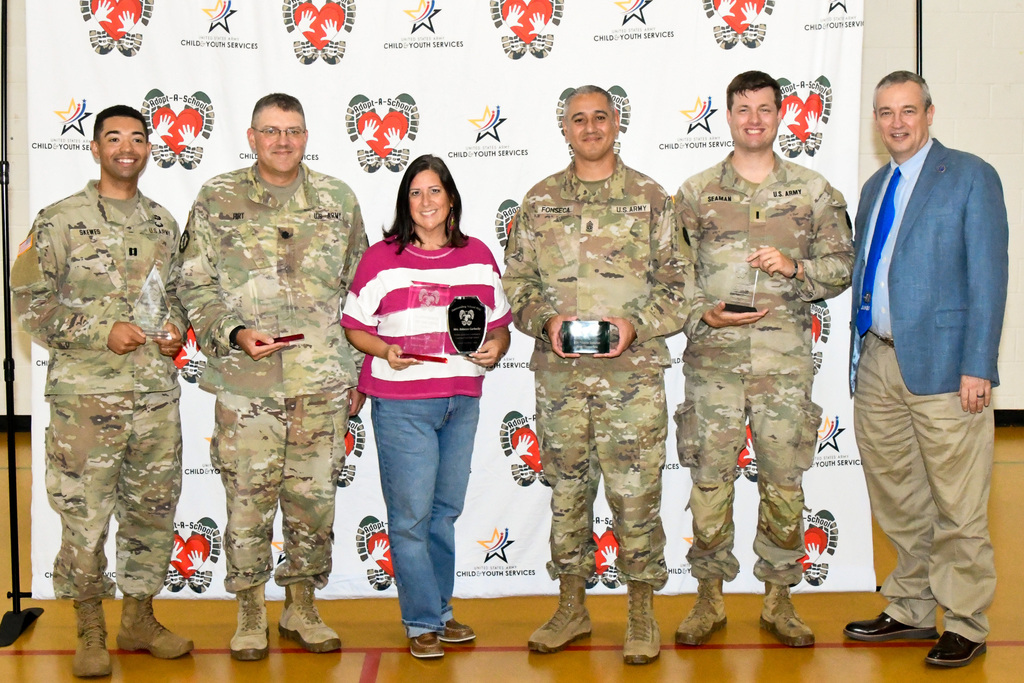 A man, woman and group of soldiers smiling and holding awards in front of a backdrop
