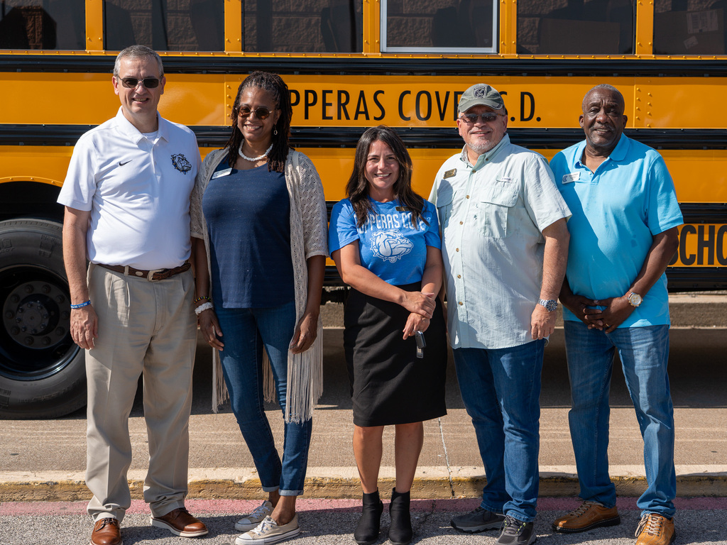 A group of people in front of a school bus smiling