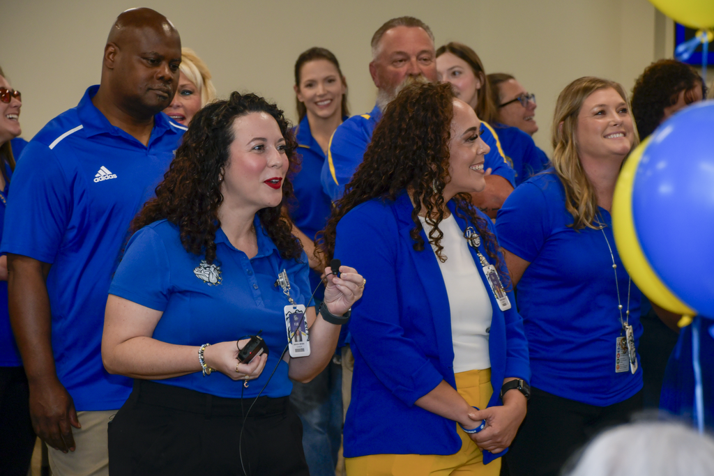 Woman talking into a microphone as others smile around her