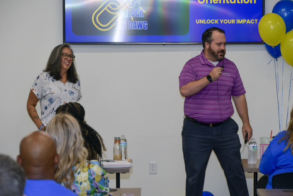 Two people laughing and speaking at the front of a room