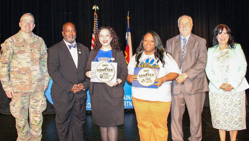 Two women and a group of dignitaries smiling, holding awards