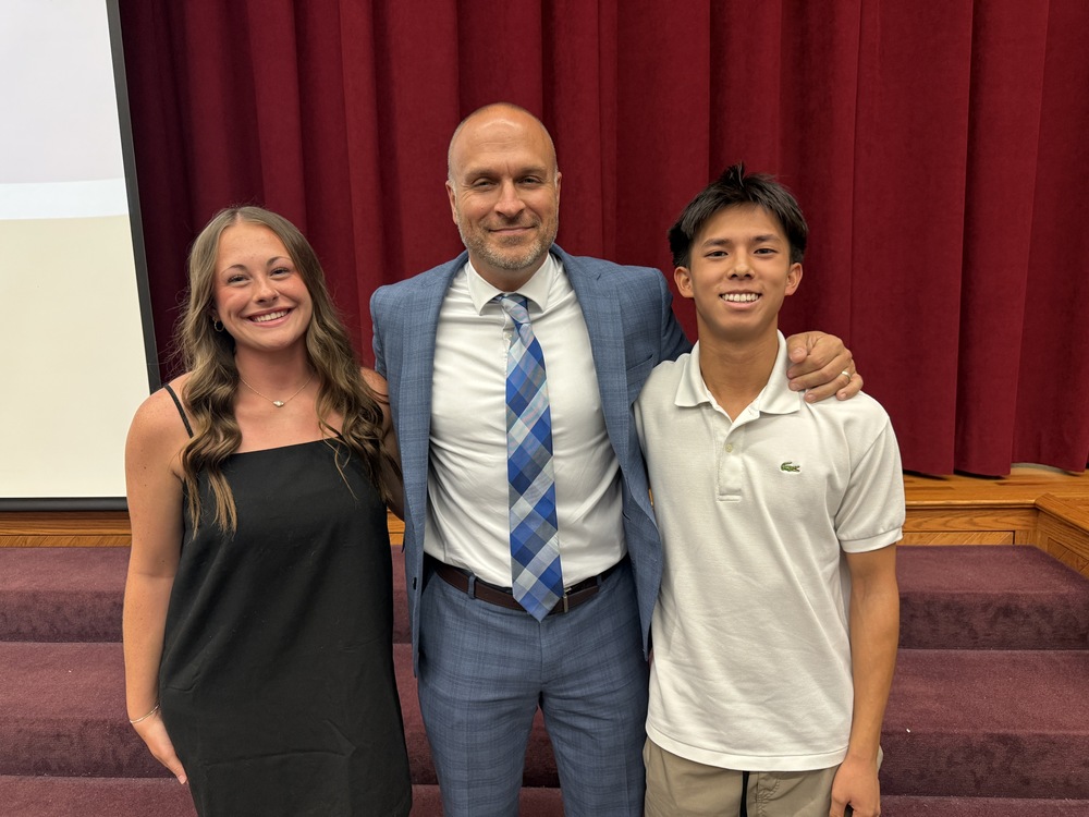 Two high school students stand in front of the stage with their high school principal