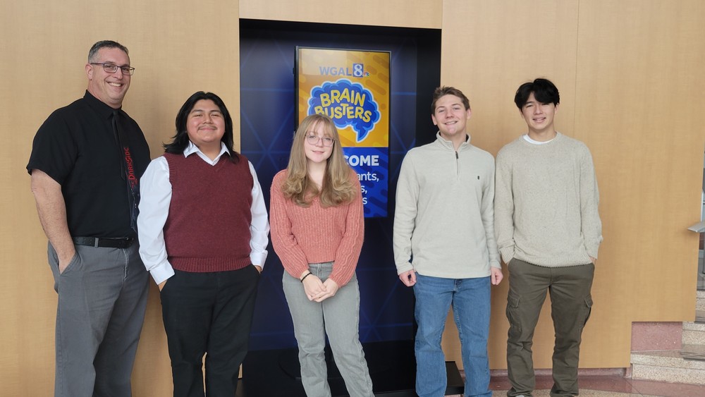 Teacher with four high school students in front of a WGAL8 Brainbusters poster