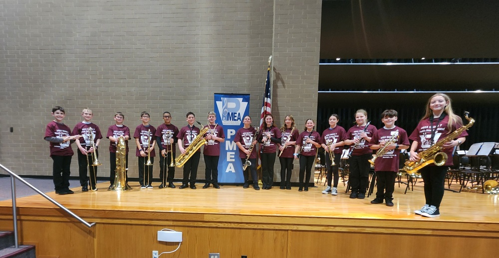 15 6th grade musicians with their instruments posing on a stage atPMEA District 7  Youth Honors Band concert