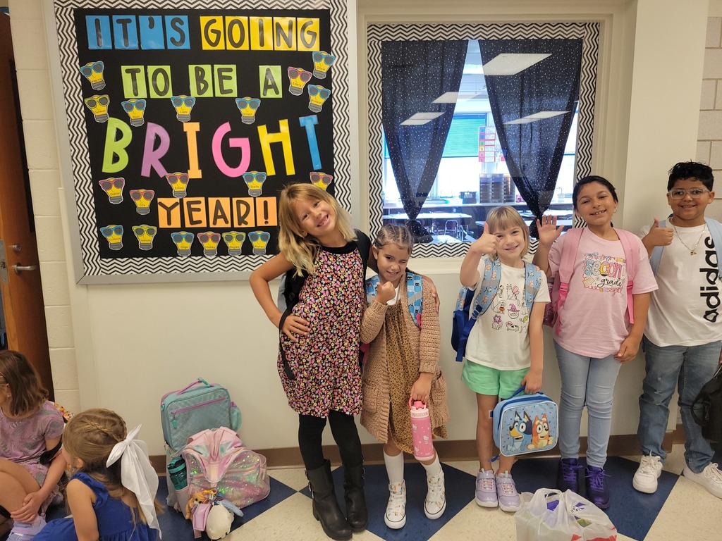 Five elementary students waving in front of their classroom