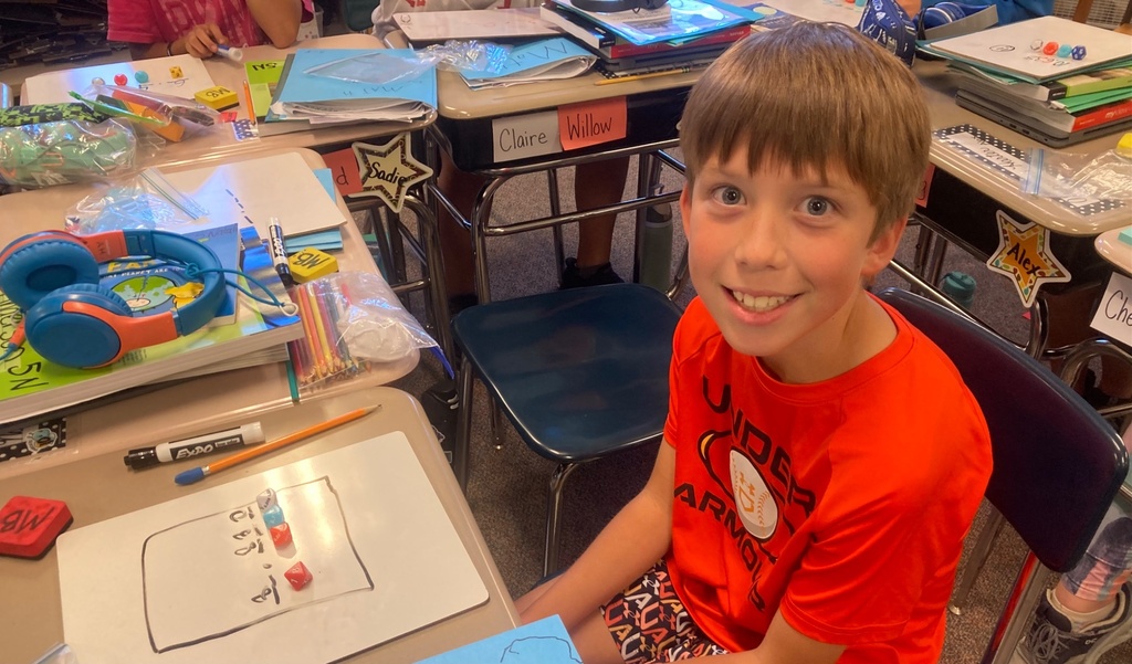 boy at desk using math maniputlatives to solve a problem on a white board