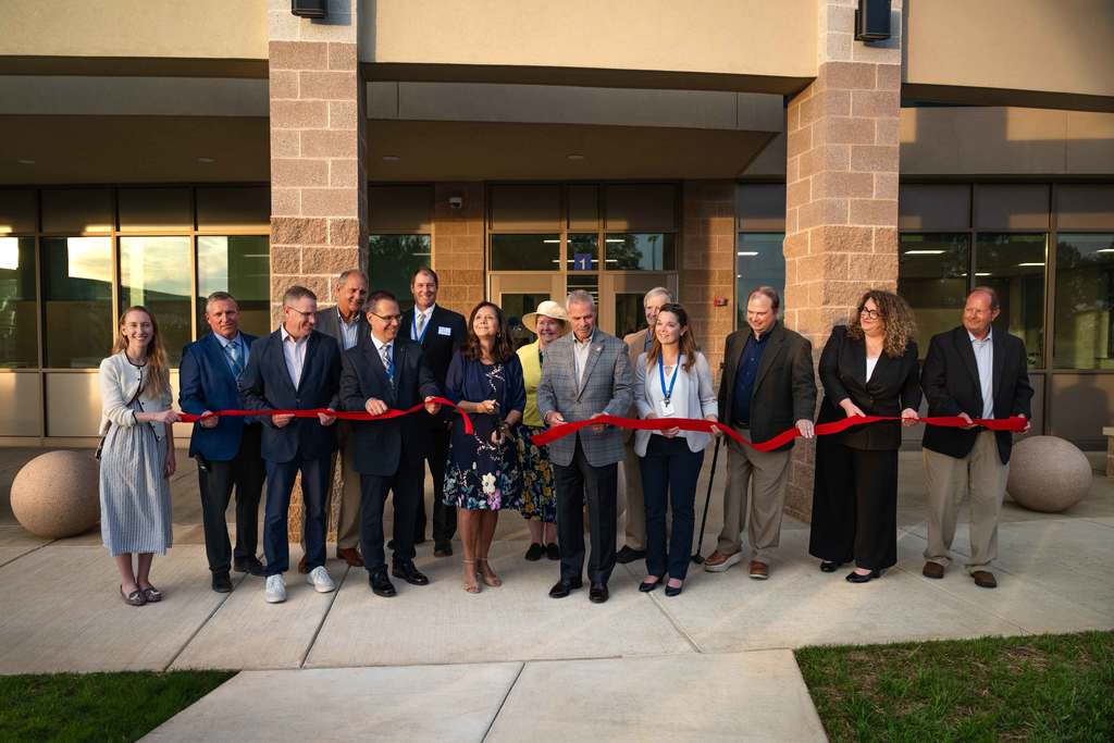 Group of people assembled to cut a red ribbon to officially open a building