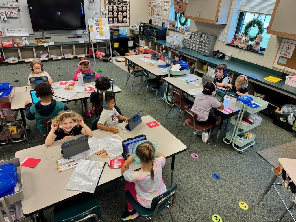 eleven young children at tables with headphones using 1:1 iPads