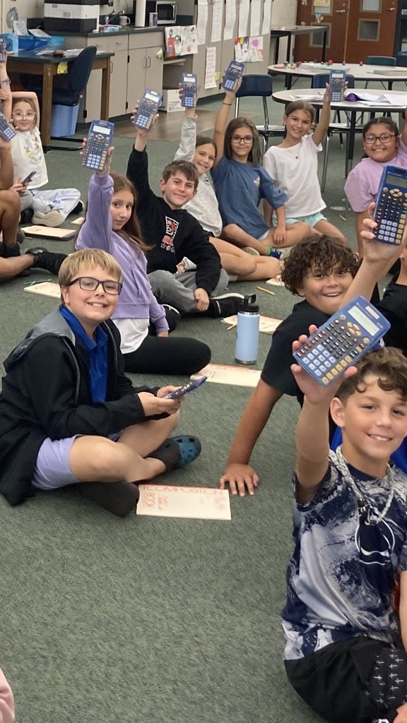 Ten smiling students sitting on the floor holding up their calculators