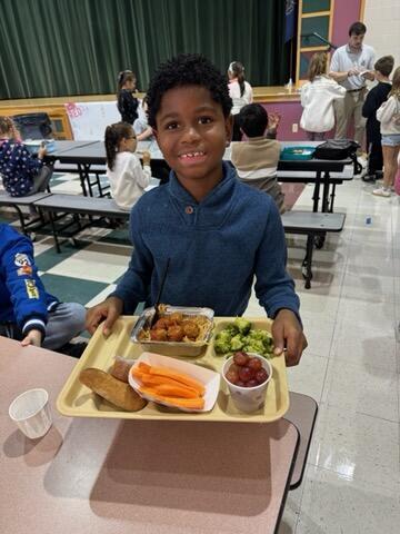 dark skinned elementary boy holding tray with colorful lunch items