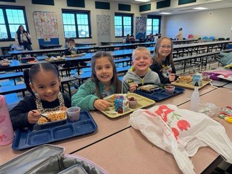4 cute kids with trays of food seated at school lunch table