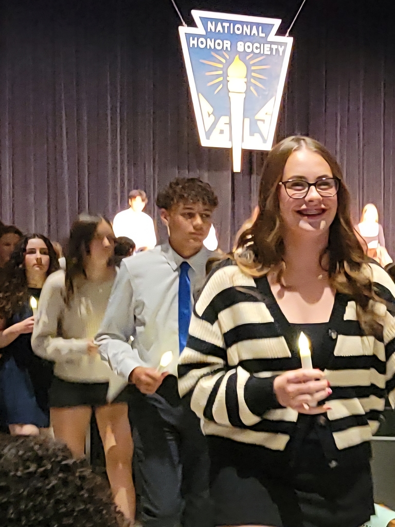 high school girl leads a line of well-dressed teens, each holding a battery operated candle, with National Honor Society sign behind them