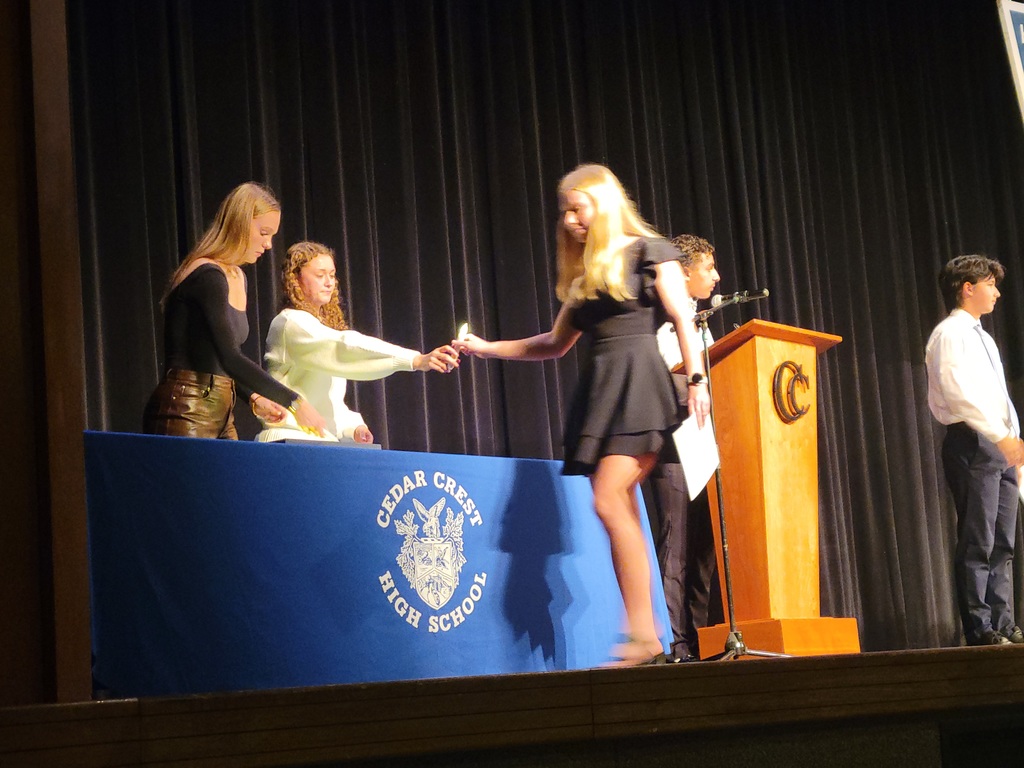 2 girls on stage behind table hand a battery operated candle to a fork in short black dress