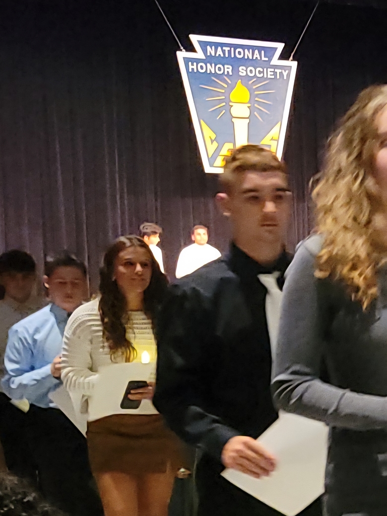 high school students, nicely dressed, walk up auditorium aisle with lit candles 