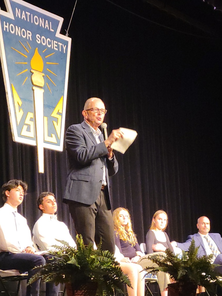 male speaker standing in front of four seated students and principal
