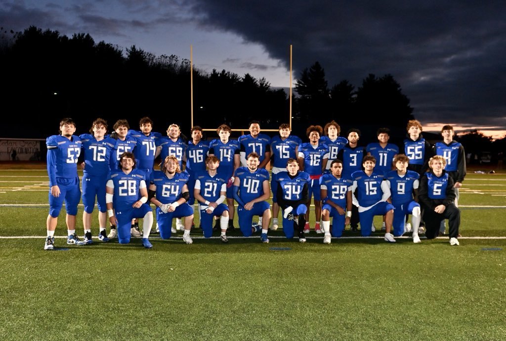 Seniors on the football team pose in their uniforms on the turf field under a darkening evening sky.