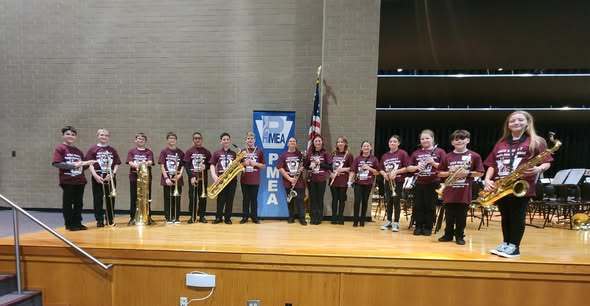 FIfteen 6th grade students musicians with their instruments on a stage before a PMEA Youth Bonors Band concert