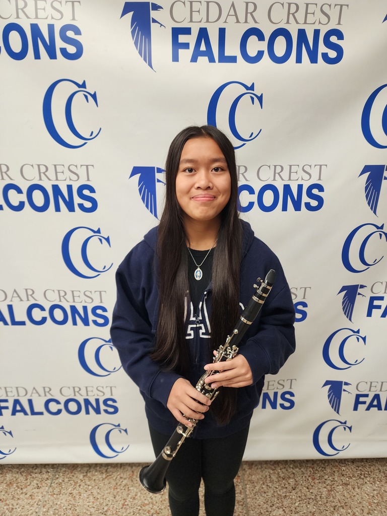 Teenager holding a clarinet in front of the Cedar Crest Falcons photo backdrop