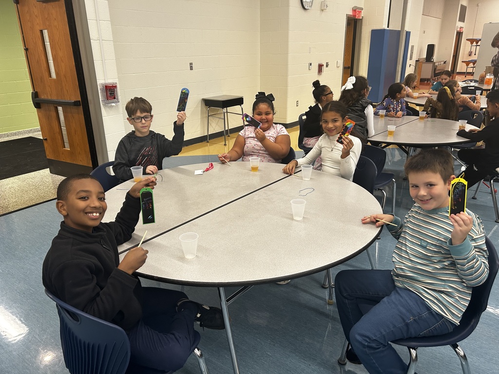 Two young girls and three young boys at a round table holding their paper craft