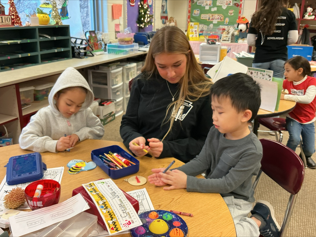 A high school girl helps two Kindergarten students make holiday crafts.