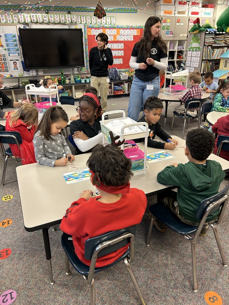 Three high school students supervise  Kindergarten students making cut-out paper crafts in their classroom