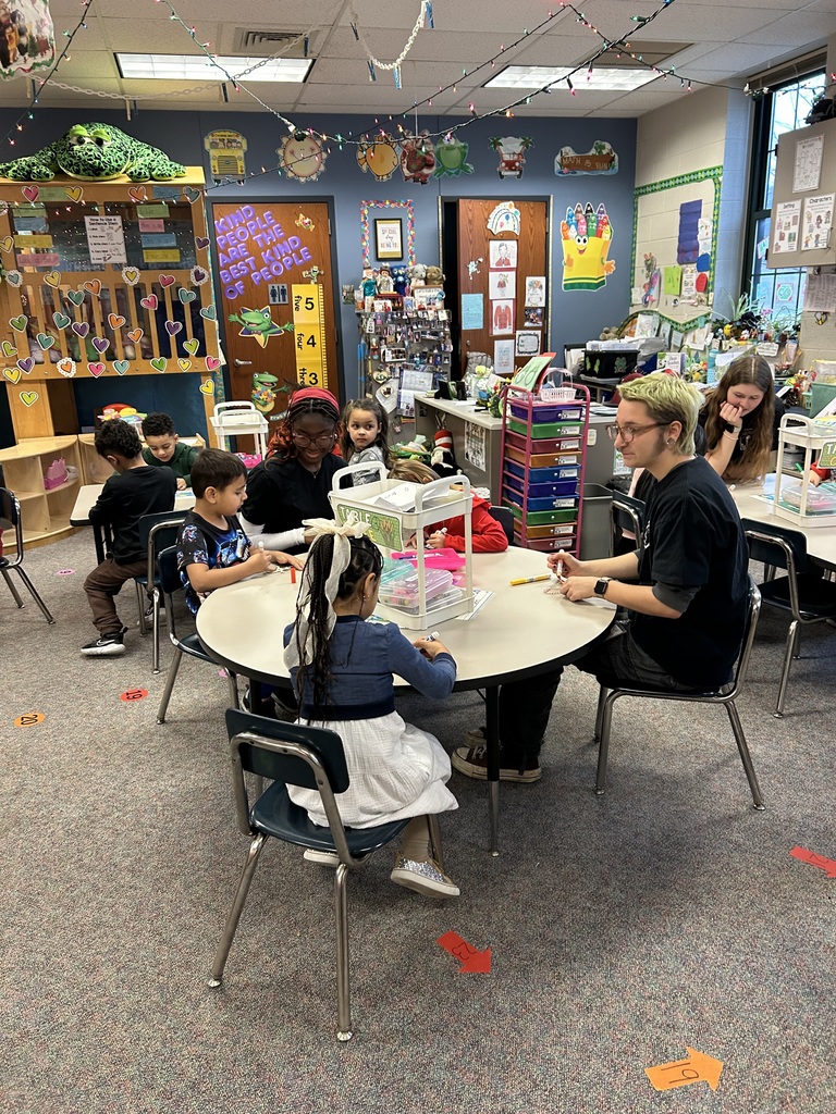 Three high school students sit at classroom tables  guiding  Kindergarten students making holiday crafts