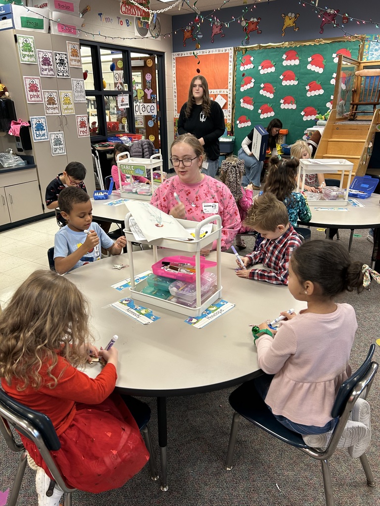 Two female high school students assist Kindergareten students coloring balsa wood holiday ornaments 