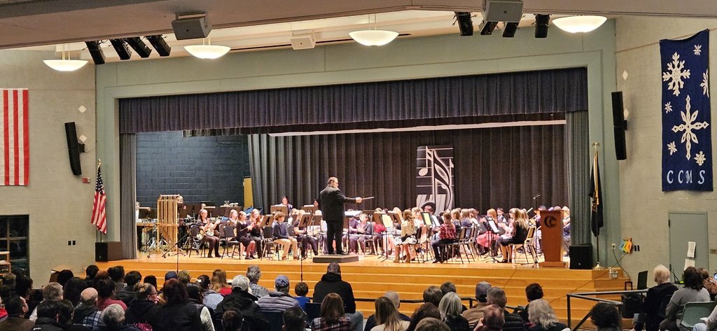 Male teacher conducting the 6th grade band performing for an audience on a school stage