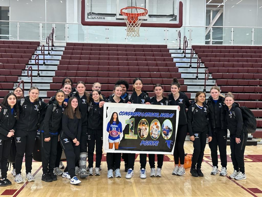girls high school basketball team holding banner celebrating Kaila Francis scoring 1,000 points