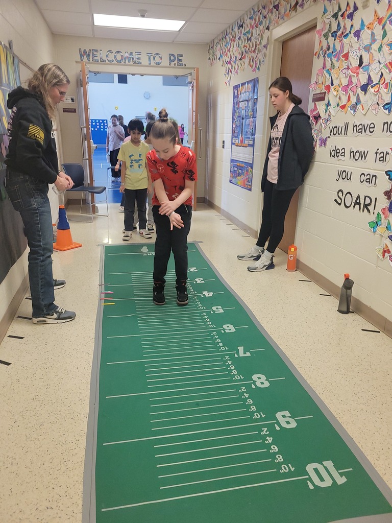 young girl lands after jumping the long jump on a green mat lined wih distances