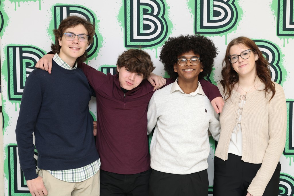 Four high school students stand in front of a banner with the Big Brothers and Big Sisters logo on it