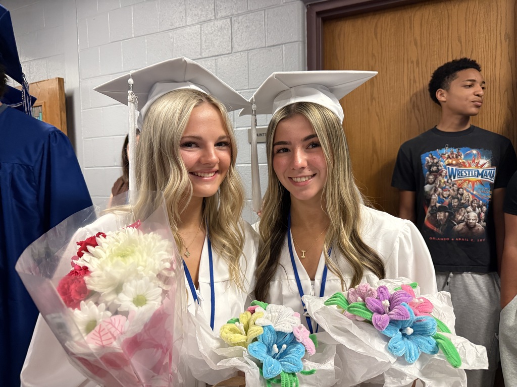Two graduating seniors pose for photos with flowers
