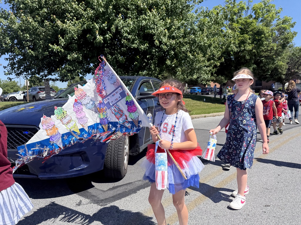 An elementary student walks in the parade with her patriotic flag