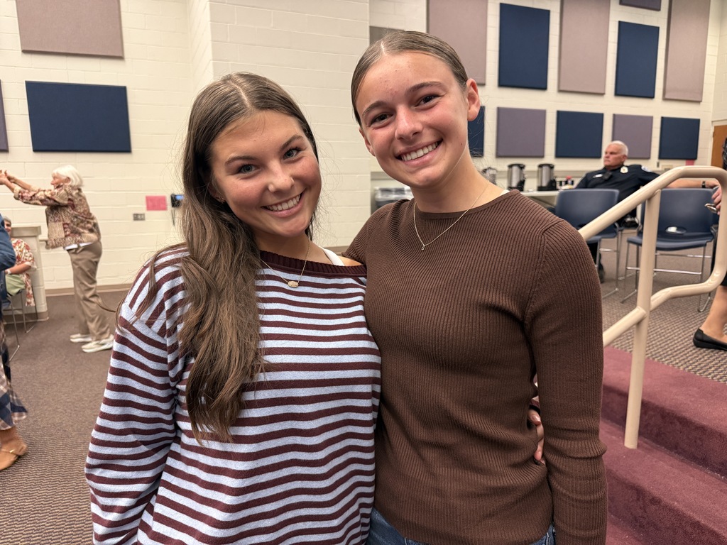 Two high school young ladies stand side by side and smile for the camera