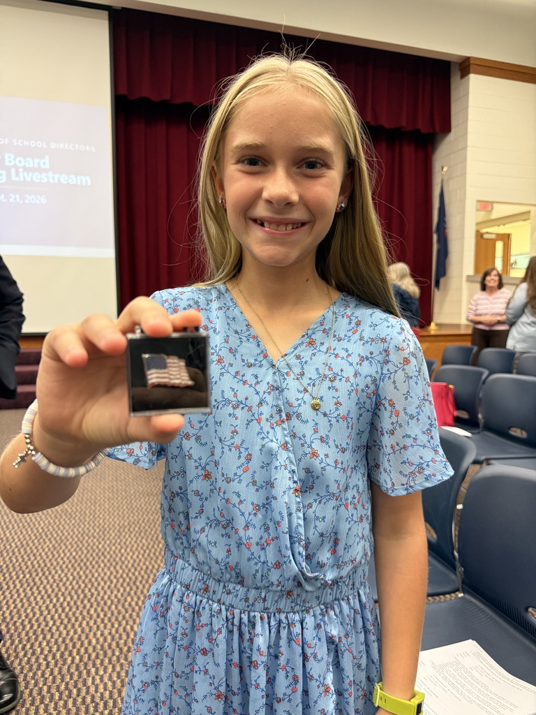A student stands in a blue dress holding out an American flag pin.
