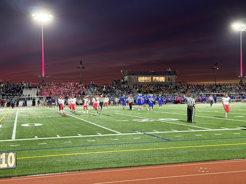 A wide shot of student-athletes on the football field at Earl Boltz Stadium with the sunset behind the press box.