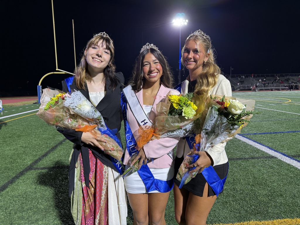 Emma Stoudt, Olivia Cuthie, and Kara Robertson wear their Homecoming crowns and hold flowers on the football field.