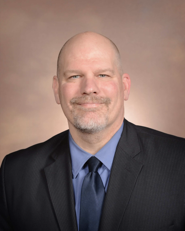 A portrait photo of Kyle Bensing in a blue shirt and tie with a sports coat