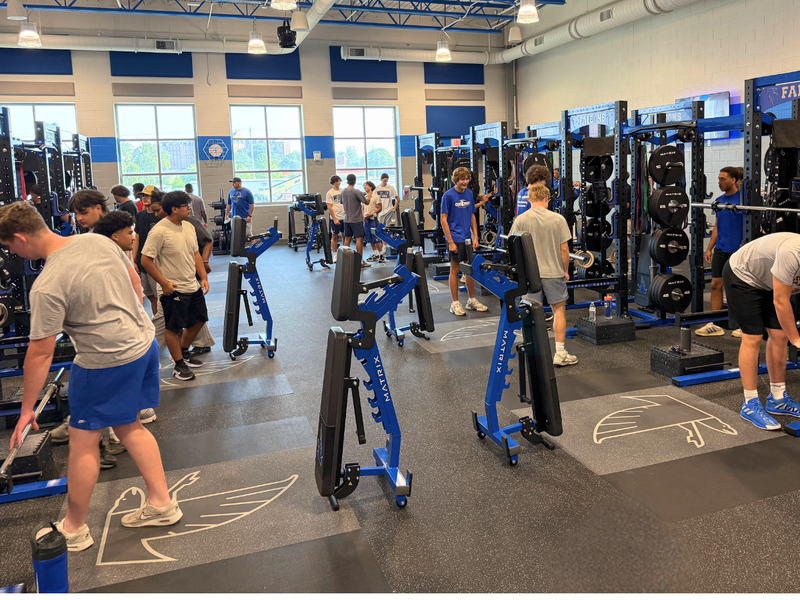 Cedar Crest High School student-athletes train throughout the renovated weight room, using blue and black strength-training equipment and weight racks.