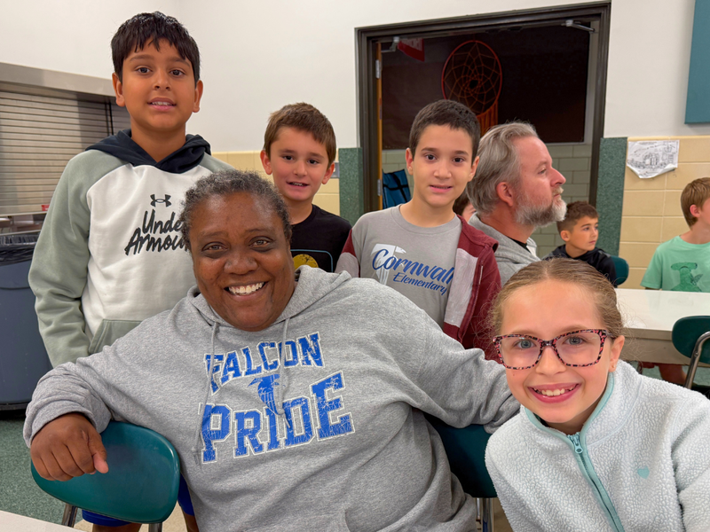 A bus driver in a Falcon Pride sweatshirt poses for a photo with four elementary students