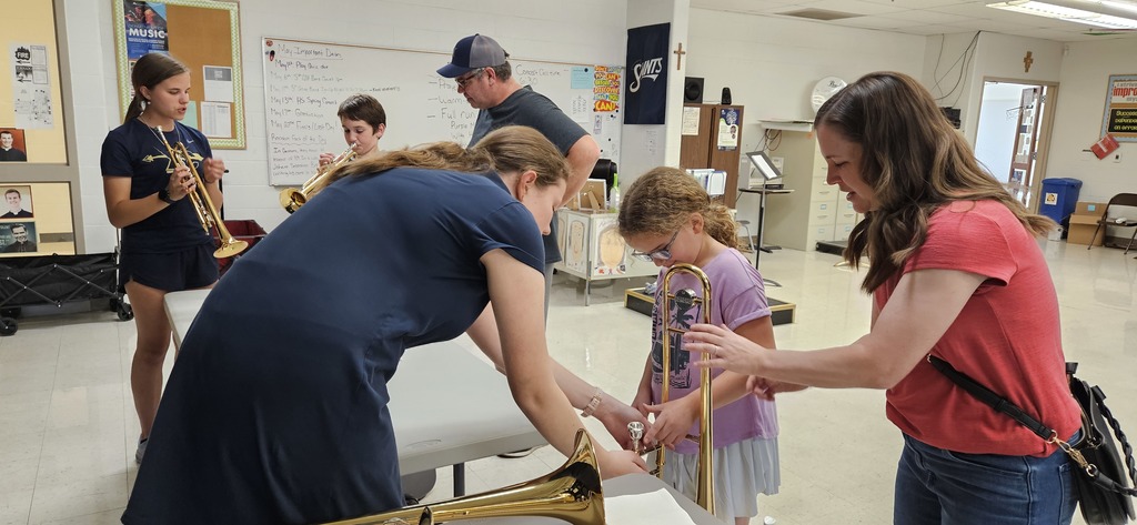 A 4th grader trying out a trombone with help from a high school student. 