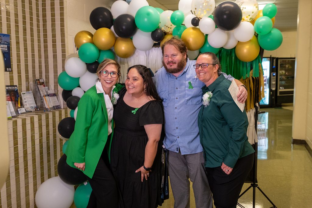 Four people pose together smiling in front of a festive balloon arch decorated in green, gold, black, and white during the Solomon M. Coles 100th anniversary celebration.