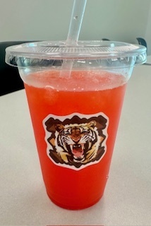 Social media post celebrating teachers at Tiger Water Bar event. Features tiger and water drop emojis with text describing how teachers have worked hard through the first 6 weeks of school - grading, planning, coaching, and inspiring students. The post announces a fun Tiger Water Bar event where staff made flavored water drinks  with names like 'Power Pounce' and 'Saratoga Sunset' to celebrate their dedication. Includes encouraging message about hydrated teachers being happy teachers, thanking CHS teachers for their energy and Tiger Pride, and motivation for the next 6 weeks. Ends with hashtags #TigerPride #RoarAndPour #TPND #EveryDayEveryClassEveryTiger.